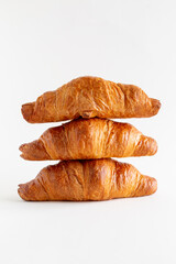 Three freshly baked croissants stacked on top of each other on a white background with copy space, vertical