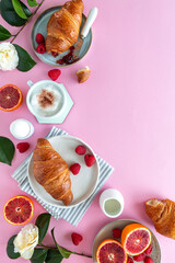 Flat lay of a breakfast scene with croissants, fruit and cappuccino on pink background