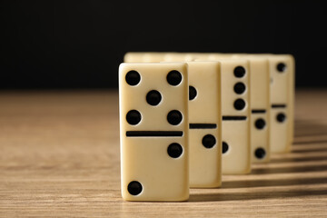 Domino tiles on wooden table against black background, closeup