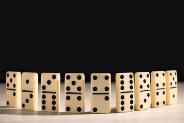Domino tiles on wooden table against black background. Space for text
