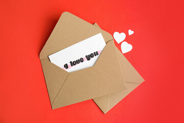 Card with phrase I Love You in envelope and paper hearts on red background, flat lay