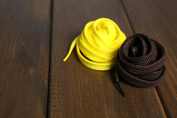 Fototapeta na wymiar Yellow and brown shoelaces on wooden background. Space for text