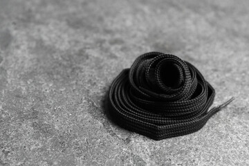 Fototapeta na wymiar Black shoelace on grey stone background. Space for text