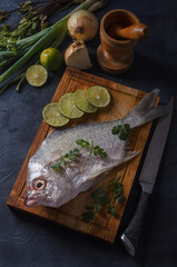Fresh fish on wooden board in black background with onion and lemon