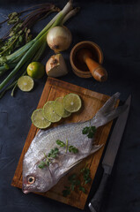 Fresh fish on wooden board in black background with onion and lemon