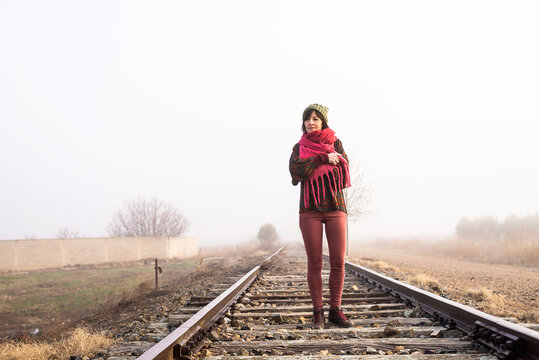 Thoughtful woman standing on a foggy railroad while looking away