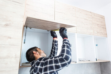 Carpenter measuring shelves that are parts of new kitchen with meter.