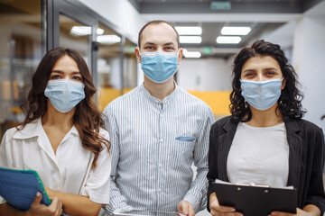 Fototapeta na wymiar Portrait of three office workers wearing medical masks discussing business and future prospects. New normal, health care, office hygiene concept. Coronavirus quarantine, pandemic, spread prevention.