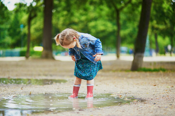 Naklejka premium Child wearing red rain boots and jumping in puddle on a summer day