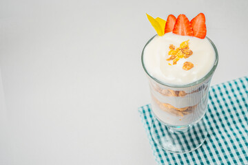 Desayuno de yogurth con fruta en copa de cristal con fresas y cereal sobre tela.