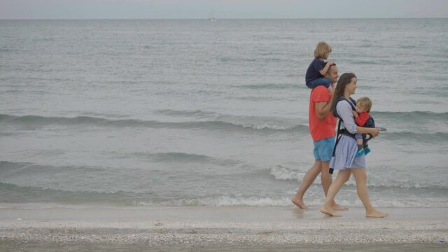 Family with tree children walk on seaside coast, baby wearing