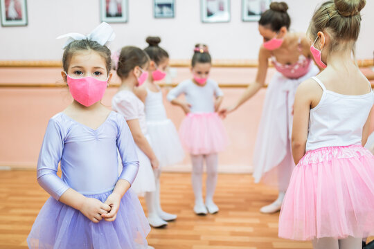 Group of beautiful little girls with protective face masks practicing ballet at dancing class. Coronavirus, Covid-19 concept.