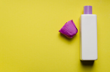 White fragrant bottle of shampoo, shower gel, purple rosebud on a yellow background. Skin and hair...