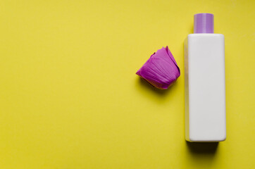 White fragrant bottle of shampoo, shower gel, purple rosebud on a yellow background. Skin and hair care. Hygiene and cosmetics. Flat lay. View from above