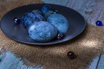 Blue Easter eggs on a dark ceramic plate on burlap on an light wooden background