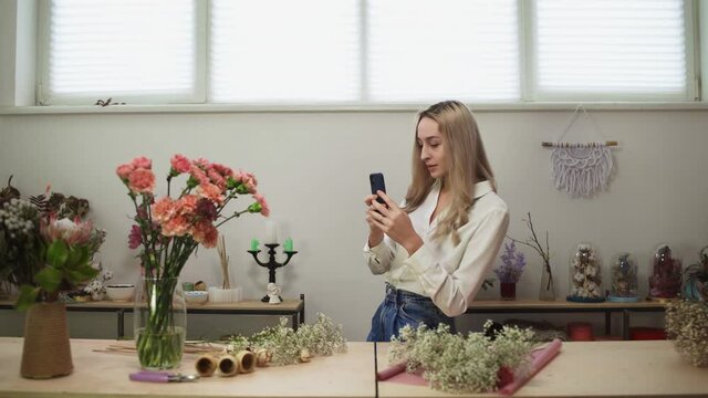 Young female florist takes photo of flowers in shop