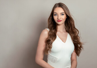 Naklejka premium Beautiful young woman with long shiny and healthy hair posing in dress on grey background
