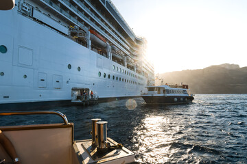 A tender boat pulls away from a large cruise ship as another docks, as the sun rises inside the...