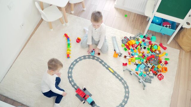 two happy young children playing at home on the railway. View from the top. cheerful little boy in the nursery playing with toys at home on the carpet on the floor. Kids games during leisure time