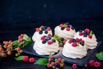 Obraz na płótnie Canvas Homemade meringue basis for cake Pavlova with fresh blueberries and BlackBerry and powdered sugar on black concrete texture background. Copy space