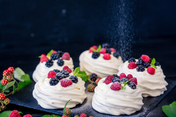 Homemade meringue basis for cake Pavlova with fresh blueberries and BlackBerry and powdered sugar on black concrete texture background. Copy space