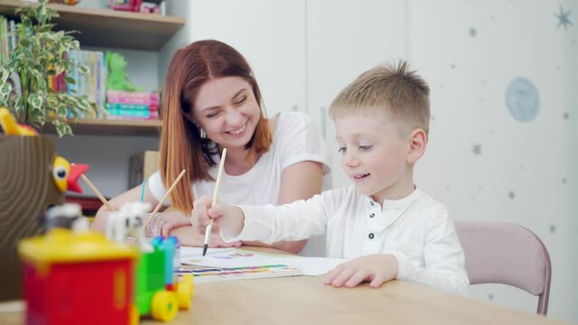 Happy family. Mom and pretty cute son are drawing at leisure at home sitting a table. Mother and preschool child spend time together. Motherhood. hobby and favorite pastime of parents in the nursery