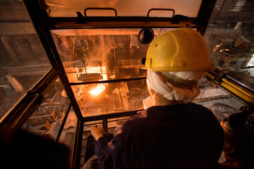 Worker operates in the cabin of a cargo crane at the steel mill