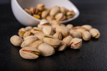 Pistachio nuts on a dark table. Salty snack in a white bowl.