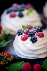 Homemade meringue basis for cake Pavlova with fresh blueberries and BlackBerry and powdered sugar on black concrete texture background. Copy space