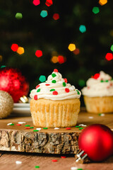 Vanilla cupcake with buttercream icing and christmas colored sprinkles on a wooden table