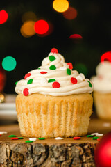 Vanilla cupcake with buttercream icing and christmas colored sprinkles on a wooden table
