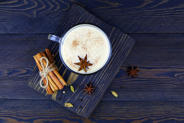 A cup of masala tea on dark wooden background. Tradition Indian tea drink with milk and spices. Top...