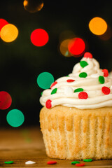 Vanilla cupcake with buttercream icing and christmas colored sprinkles on a wooden table