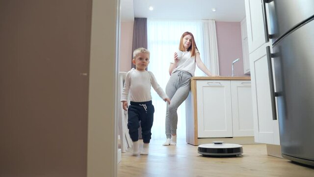 woman enjoys a robot vacuum cleaner. Young female is resting while cleaning the house. controls a using a smartphone app at home. young housewife easily and simply cleans the apartment
