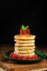 stack of buttermilk pancakes with raspberries and mint topped with honey