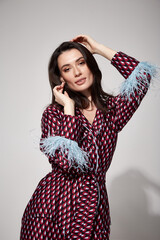 Pretty sexy woman beautiful face natural makeup brunette hair wear silk textile suit pants and blouse with feathers shoes comfort casual home dress luxury lifestyle pajama party glamour fashion model.