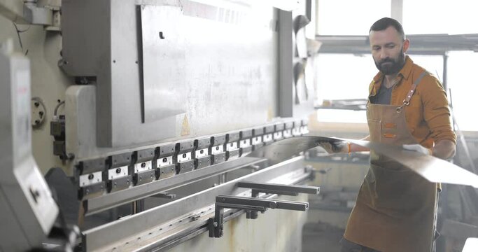Factory worker controlling the process of bending metal sheets at the manufacturing