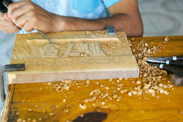 Manos de un hombre tallando con gubias sobre madera, trabajo artesanal 