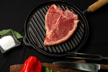 beef steaks on rustic board and metal plate with pepper shakers, garlic, spices, knife and grill fork