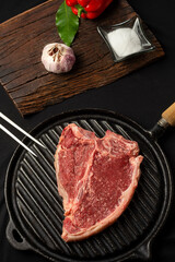 beef steaks on rustic board and metal plate with pepper shakers, garlic, spices, knife and grill fork