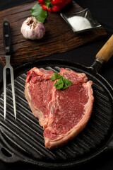 beef steaks on rustic board and metal plate with pepper shakers, garlic, spices, knife and grill fork