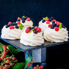 Homemade meringue basis for cake Pavlova with fresh blueberries and BlackBerry and powdered sugar on black concrete texture background. Copy space - 408684145