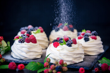 Homemade meringue basis for cake Pavlova with fresh blueberries and BlackBerry and powdered sugar on black concrete texture background. Copy space - 408684755