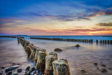 sunset at the baltic sea with cross groynes, stones and clouds. beautiful frbenfroher sky, long time exposure 