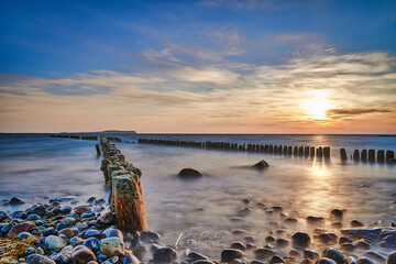 sunset at the baltic sea with cross groynes, stones and clouds. beautiful frbenfroher sky, long time exposure 