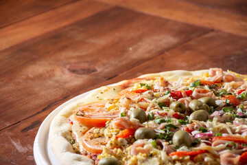 Delicious pizza with ham, cheese, tomato, egg and olives on rustic wooden table.