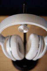 White wireless head large headphones stand on a wooden table on a black stand on a blue background top view