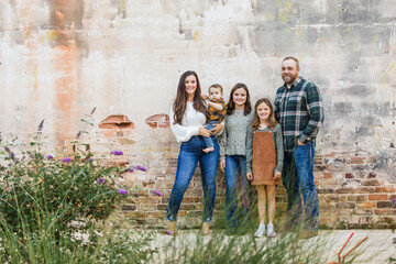 A family of five with two girls and a baby boy standing by an urban old brick wall