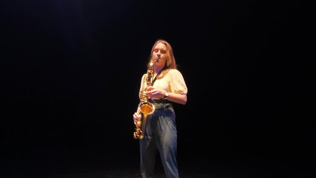 Young Woman Musician Playing Solo on Saxophone Under Lights on Dark Stage