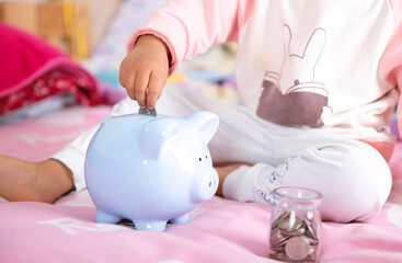 Little yellow child hand puts dollar coins into piggy bank
